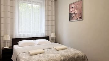Een hotelkamer met een bed, twee bedlampen, een raam met gordijnen en een aan de muur hangend schilderij.