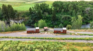 Landskab med huse og en mindre lade, omgivet af tæt skov og en flod.