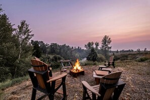 An outdoor seating area with chairs and a fire pit, surrounded by trees and a view of the landscape. - Peaceful Riverfront Cabin with Scenic Outdoor Deck in Ashton, Idaho (Ashton)