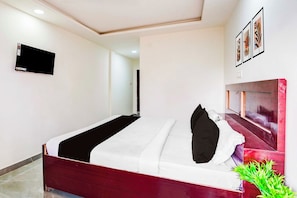 Ein Hotelzimmer mit einem Bett, einem an der Wand befestigten Fernseher und einer Pflanze auf dem Boden.