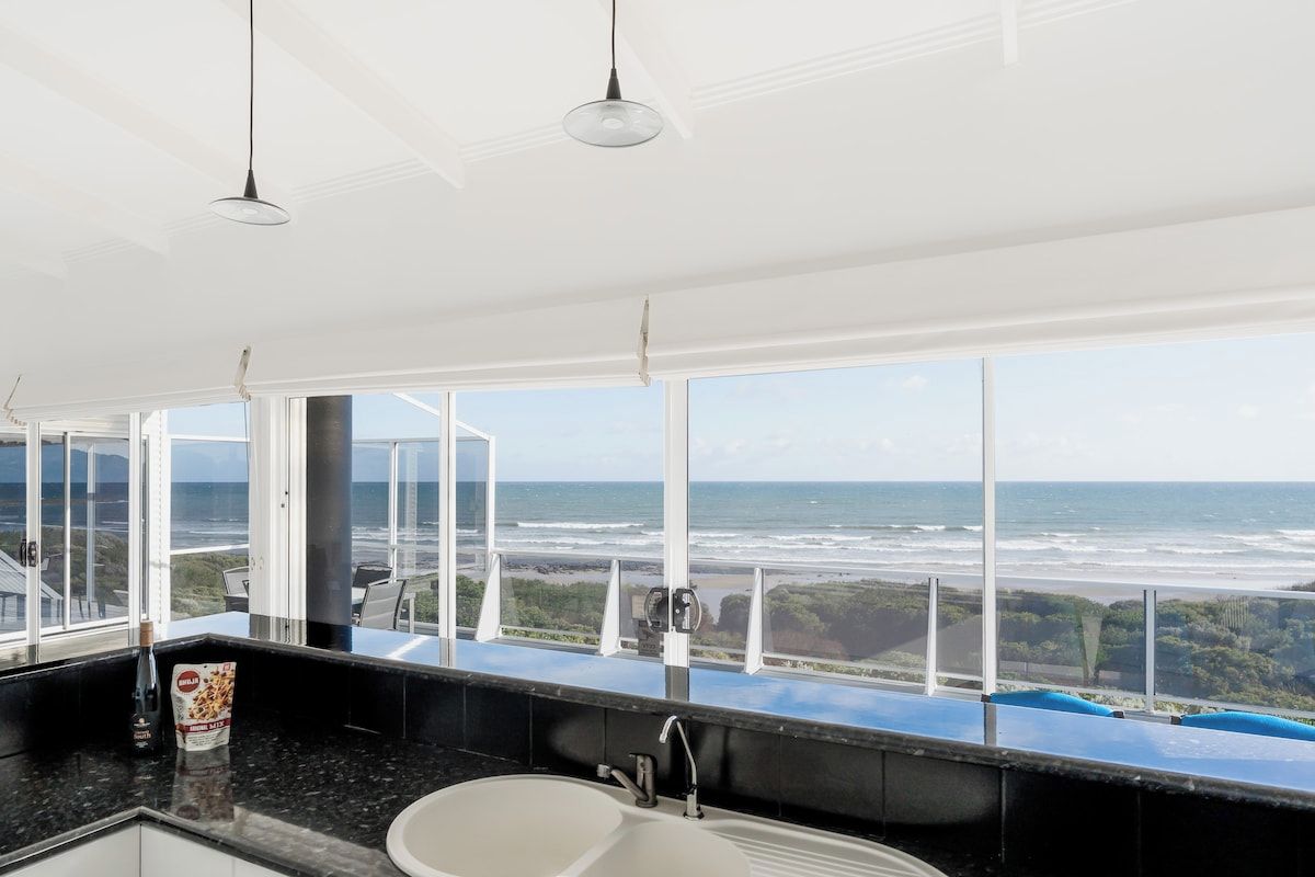 A bathroom with a large window, a sink, and a bottle of shampoo.