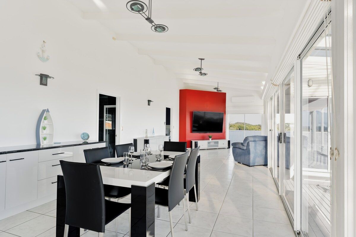 A modern kitchen with white cabinets, a dining area with black chairs, and a red accent wall.