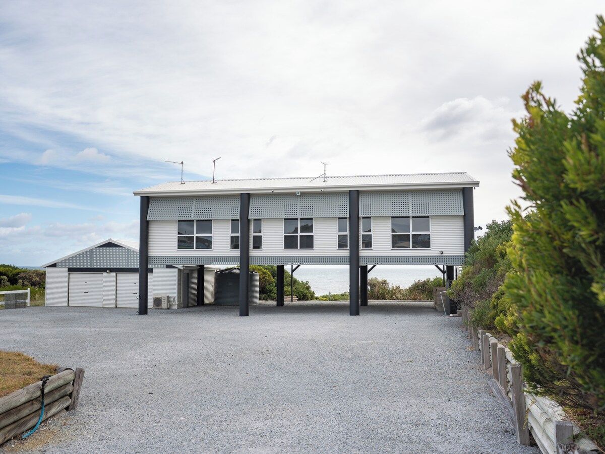 A two-story building with a flat roof, large windows, and a gravel driveway.