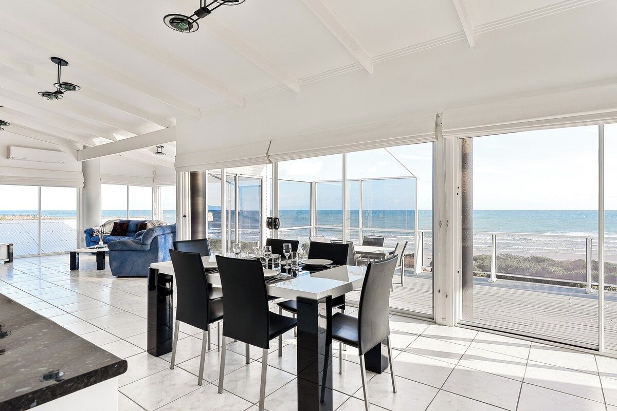 A spacious dining area with a view of the ocean, modern furniture, and large windows.