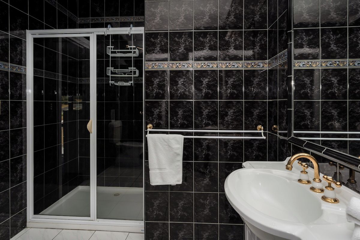 A bathroom with a glass-enclosed shower, a white sink with gold fixtures, and dark marble tiles.