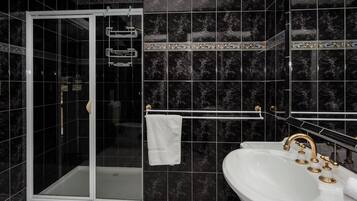 A bathroom with a glass-enclosed shower, a white sink with gold fixtures, and dark marble tiles.