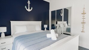 A bedroom with a bed, nightstands, a dresser, a mirror, and wall-mounted decor. - Shack Vibes, Direct Beach Access (Low Head)