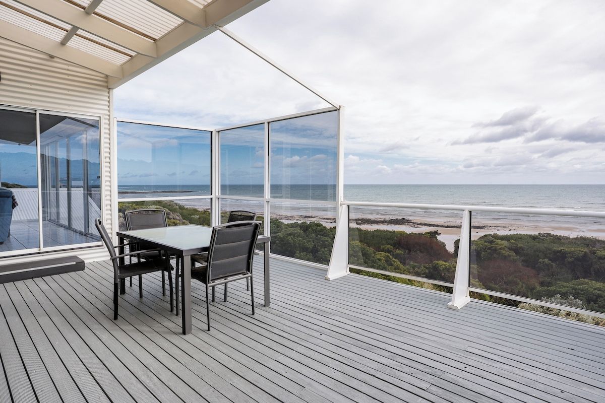 A deck with a table and chairs overlooking a beach and forest.