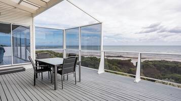A deck with a table and chairs overlooking a beach and forest.