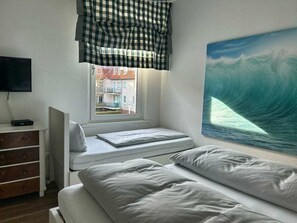 Una camera da letto con un letto, una cassettiera, una finestra che mostra edifici e un quadro raffigurante un'onda.