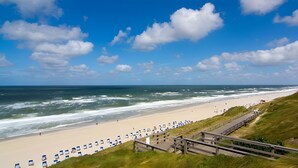 A beach with a wooden boardwalk leading to beach chairs and umbrellas. - Apartment 'Sternengucker Sylt' with Balcony and Wi-Fi (Wenningstedt-Braderup (Sylt))