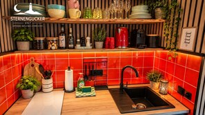 A kitchen with a red tiled backsplash, wooden shelves, and various kitchen utensils.