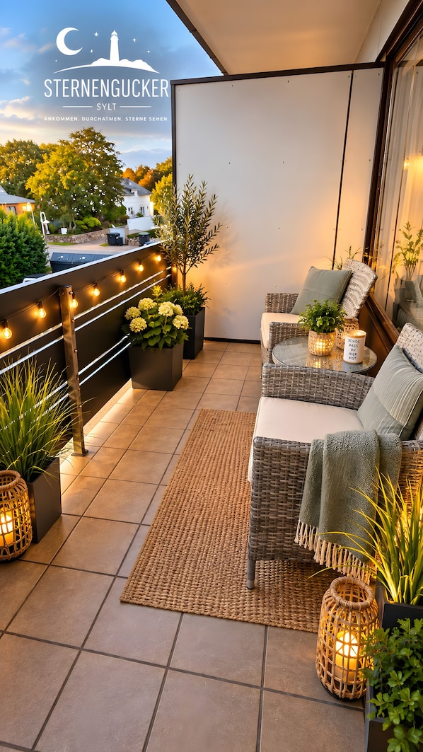 A balcony with outdoor seating, potted plants, and string lights.
