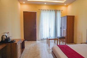 Habitación de hotel con cama, escritorio con hervidor, silla, armario y ventana con cortinas.