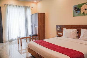 Una habitación de hotel con cama, escritorio, silla, armario y un cuadro en la pared.