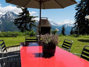 A red table with a potted plant, outdoor chairs, and an umbrella. - Sportina 21 2. OG Süd-Ost Appartement/Fewo, Bad, WC by Interhome (Riederalp)