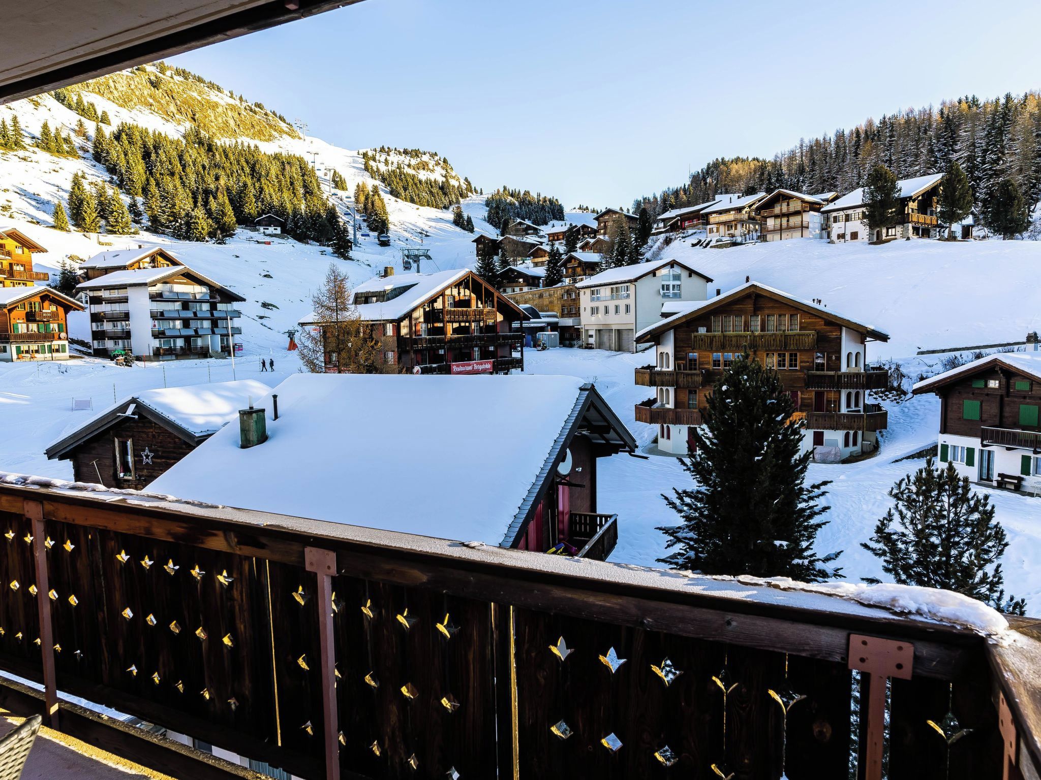 Un pueblo cubierto de nieve con edificios de madera, incluyendo un hotel con balcones y un restaurante.