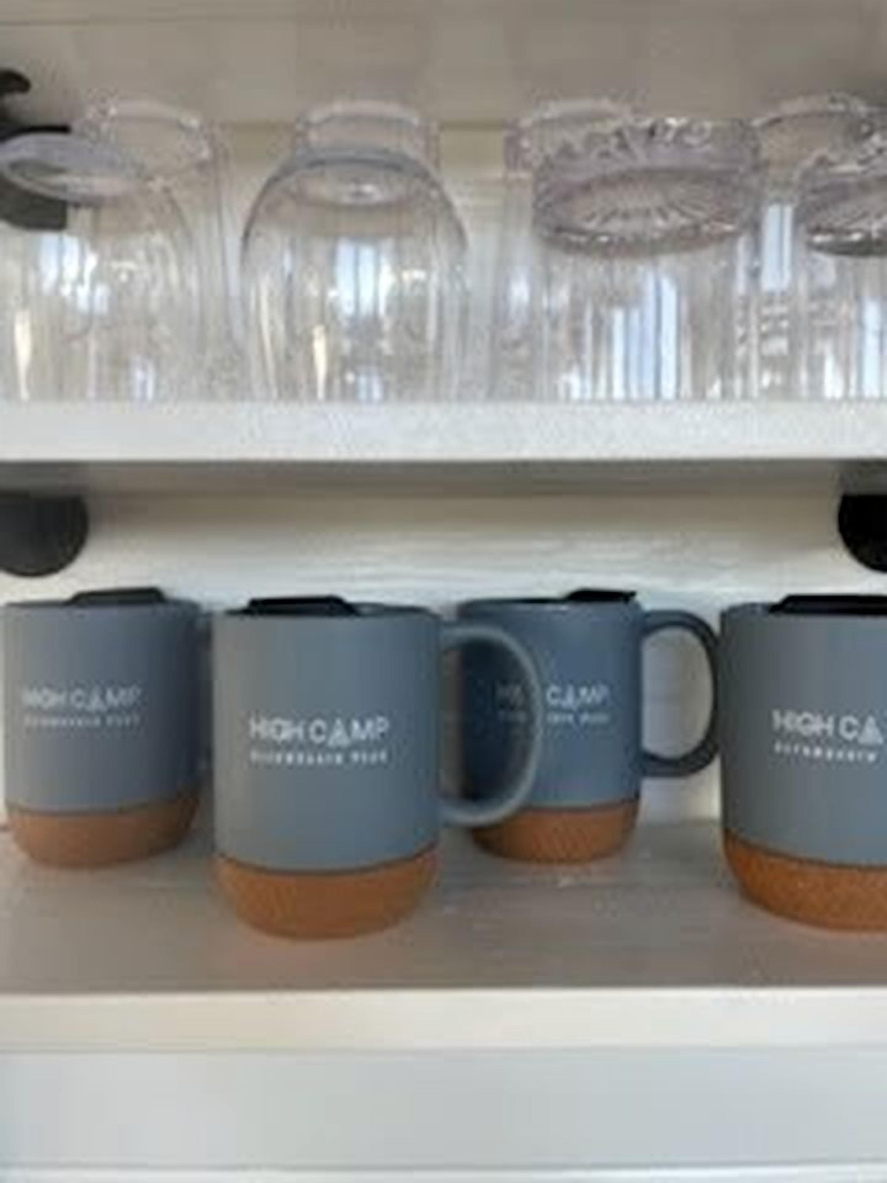 A shelf with clear glass tumblers and grey mugs with brown bases.