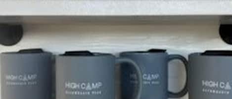 A shelf with clear glass tumblers and grey mugs with brown bases.