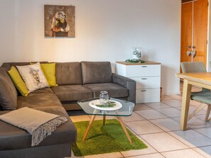 A modern living room with a grey sofa, a glass coffee table, a white side table, and a dining area with a wooden table and chairs. - Sportina 12 1. OG Süd Appartement/Fewo, Dusche, WC by Interhome (Riederalp)