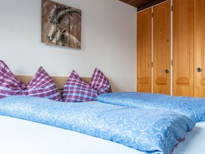 A bedroom with a bed, checkered pillows, a blue patterned bedspread, a wooden wardrobe, and a painting of an animal on the wall. - Sportina 12 1. OG Süd Appartement/Fewo, Dusche, WC by Interhome (Riederalp)