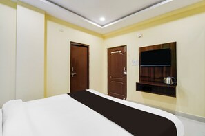 A hotel room with a bed, two doors, a television mounted on the wall, and a small shelf with a kettle. - Super Townhouse Hitech City Madhapur (Hyderabad)