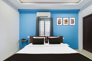 Habitación de hotel con cama, ventana con cortinas, aire acondicionado de pared y tres cuadros enmarcados.