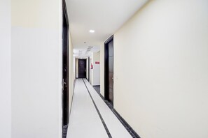 A corridor with a fire exit sign, a door at the end, and a tiled floor. - Townhouse Sector 51 Noida (Noida)
