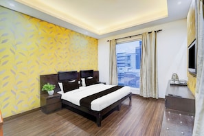 Een moderne hotelkamer met een groot bed, een nachtkastje met een plant, een televisie en uitzicht op de stad door het raam.