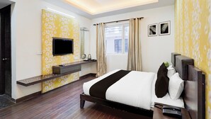 Een hotelkamer met een bed, een televisie, een nachtkastje, een raam met gordijnen en een muur met een bloemenmotief.