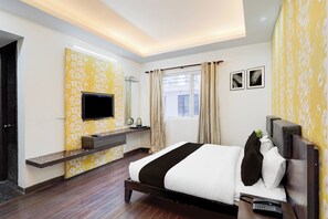 Habitación de hotel con cama, televisión, mesita de noche, ventana con cortinas y pared con estampado floral.