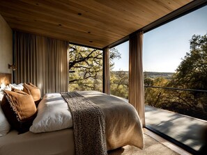 A bedroom with a large bed, curtains, and a view of trees and hills. - Off-Grid Mirrored Glass House Above the Lake with Stargazing & Hill Country Views in Marble Falls, Texas (Marble Falls)