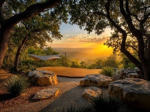 A wooden deck with a canopy, surrounded by rocks and plants, overlooking a landscape. - Off-Grid Mirrored Glass House Above the Lake with Stargazing & Hill Country Views in Marble Falls, Texas (Marble Falls)