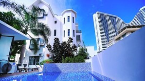 Piscina com piso azulejado, cercada por edifícios modernos e vegetação.