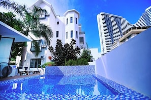 Una piscina con piso de baldosas, rodeada de edificios modernos y follaje.