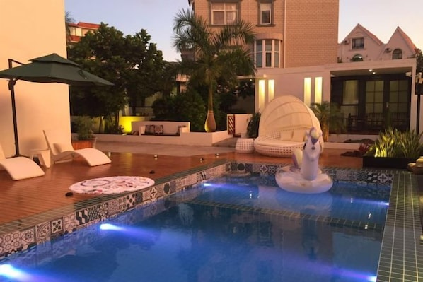 Un área de piscina con sillas de descanso, una fuente decorativa y un suelo de baldosas.