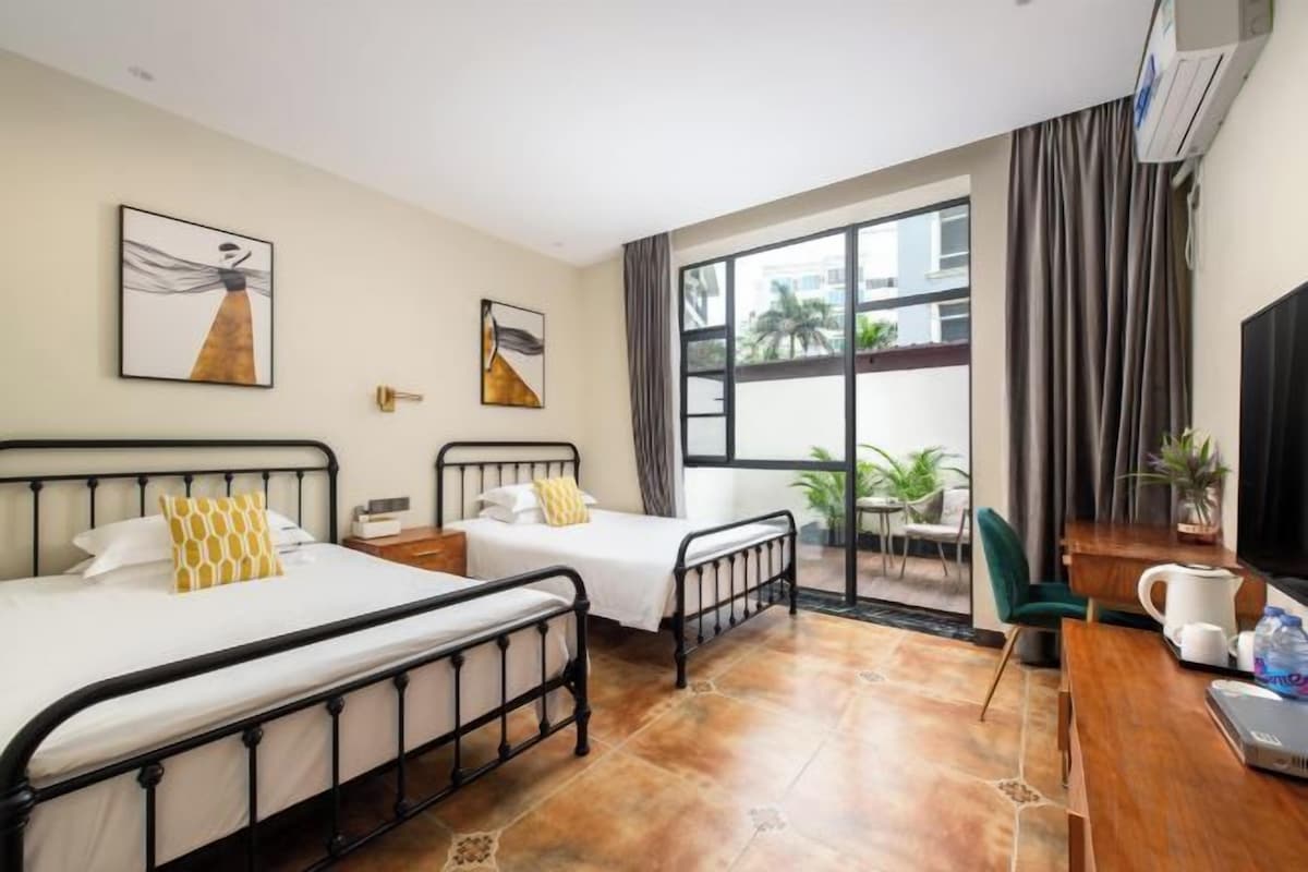 Habitación de hotel con dos camas, un escritorio, una silla, un televisor y un ventanal grande.