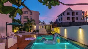 Piscina com espreguiçadeiras e hidromassagem, cercada por edifícios e palmeiras.