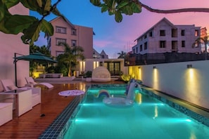 Una piscina con sillas de descanso y un jacuzzi, rodeada de edificios y palmeras.