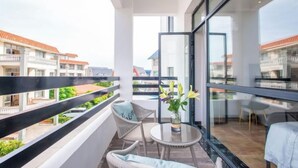 Uma varanda com móveis de vime, uma mesa pequena com um vaso e vista para edifícios vizinhos.