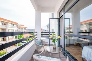 Un balcón con mobiliario de mimbre, una mesita con un florero y vistas a edificios cercanos.