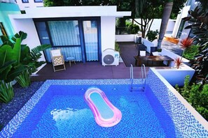 Una piscina con escalera, rodeada por un patio con asientos y un ventilador.
