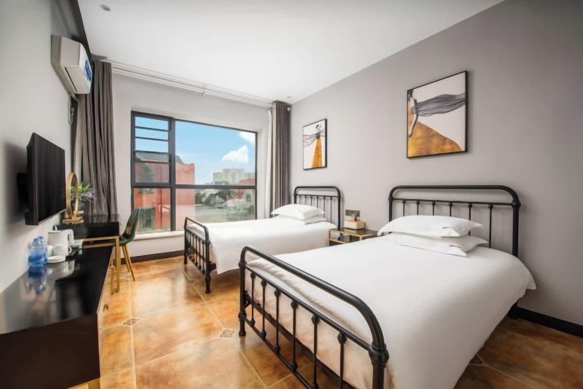 Habitación de hotel con dos camas, un escritorio, una silla, un televisor y una ventana con vista a la ciudad.
