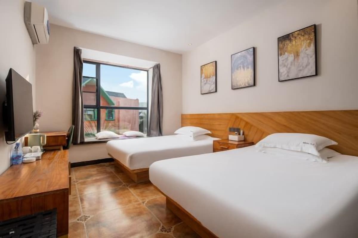 Habitación de hotel con dos camas, un escritorio, un televisor de pantalla plana, una ventana con cortinas y obras de arte en las paredes.