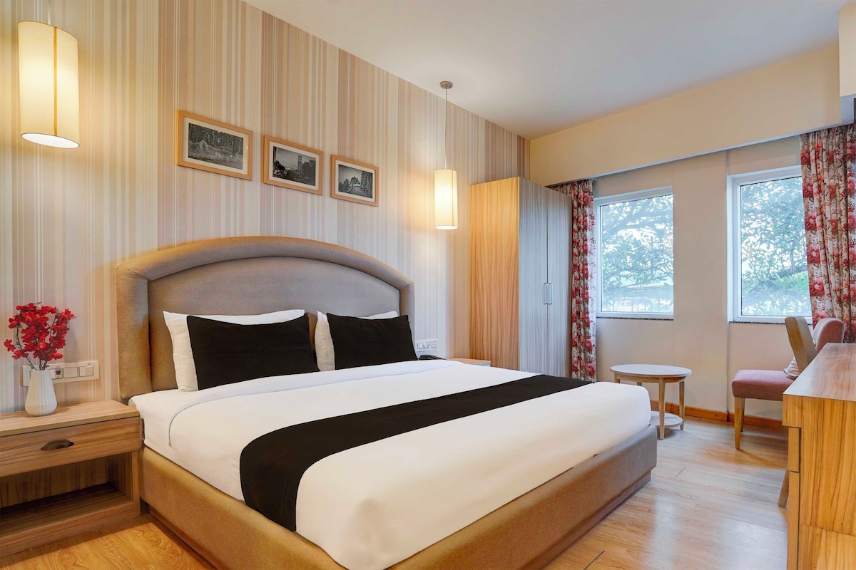 Une chambre d’hôtel avec un grand lit, des lampes de chevet, une petite table, une chaise et une fenêtre avec des rideaux.