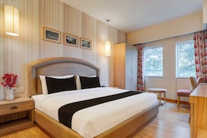 Une chambre d’hôtel avec un grand lit, des lampes de chevet, une petite table, une chaise et une fenêtre avec des rideaux.
