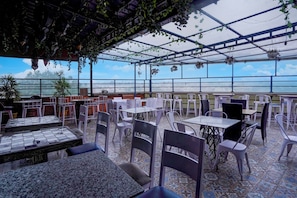 Un café en plein air avec des tables et des chaises, un sol carrelé et des plantes suspendues.