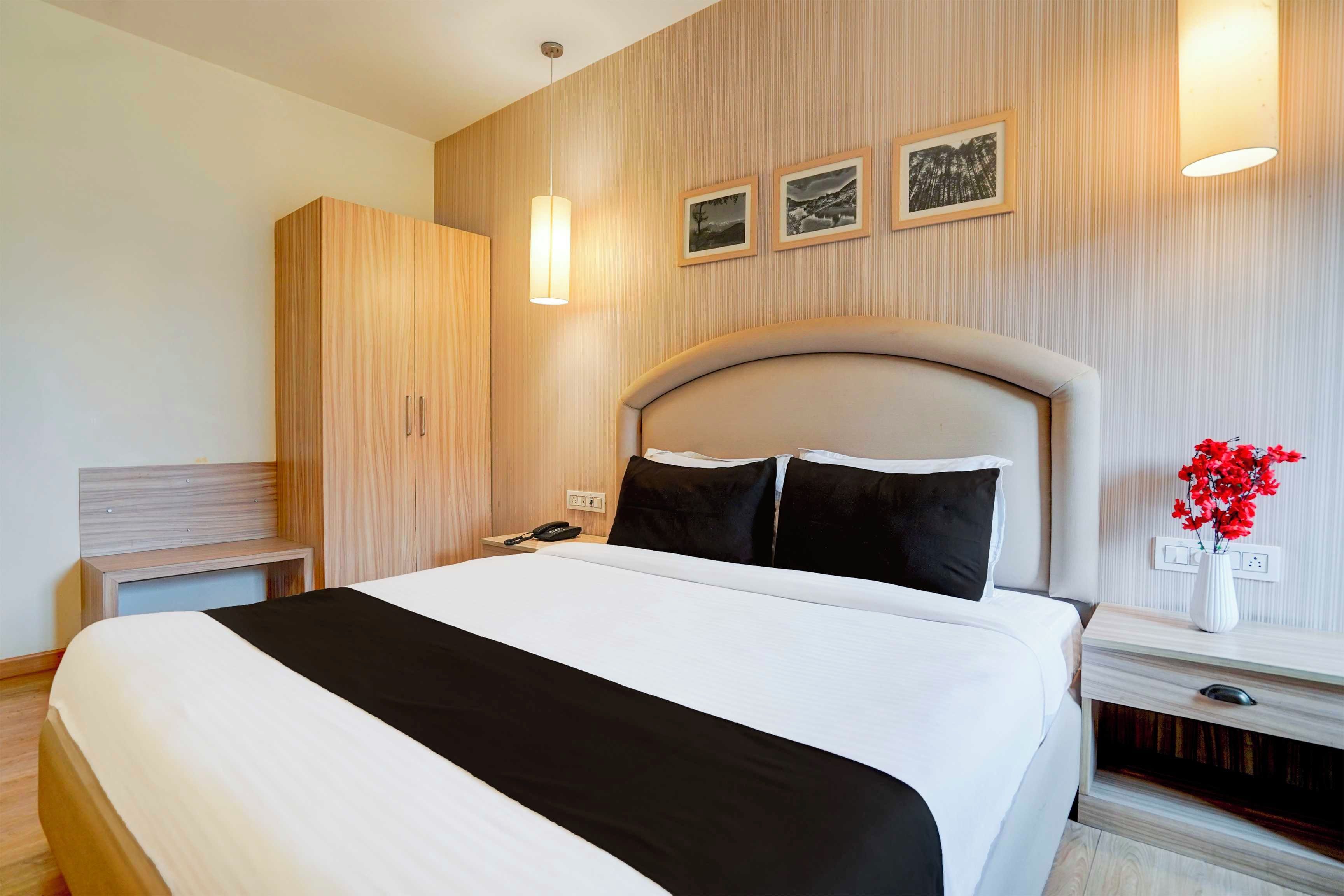 Een moderne hotelkamer met een groot bed, een kledingkast, een nachtkastje met lamp en een telefoon aan de muur.