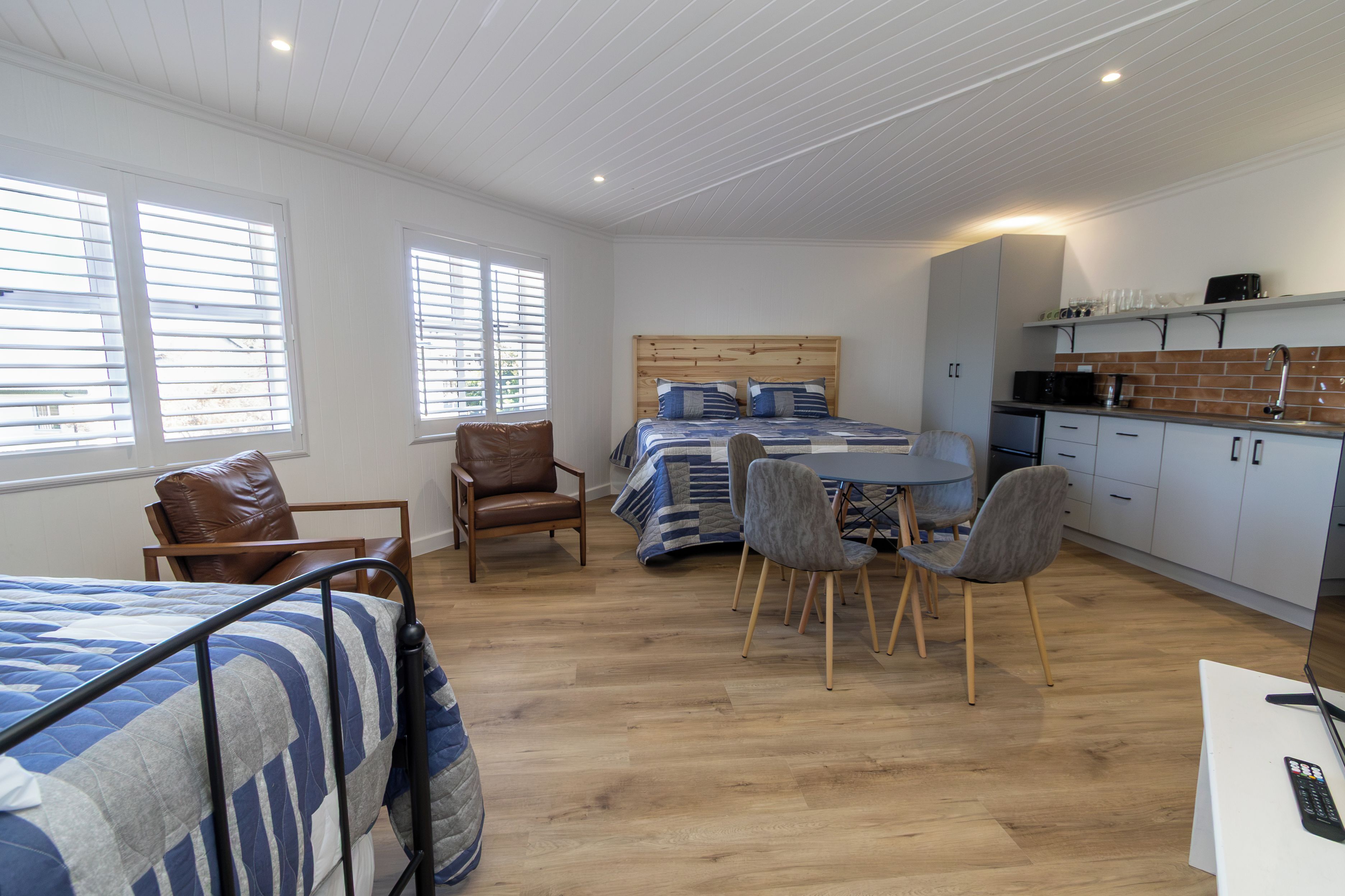 Een kamer met een bed, een bureau, een stoel, een kitchenette en een raam.
