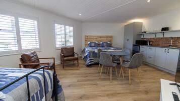 Een kamer met een bed, een bureau, een stoel, een kitchenette en een raam.